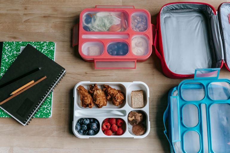 Lunch boxes filled with healthy meals placed next to notebooks on a table.