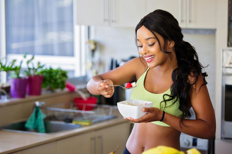 Woman eating a fresh strawberry in a bright kitchen setting.